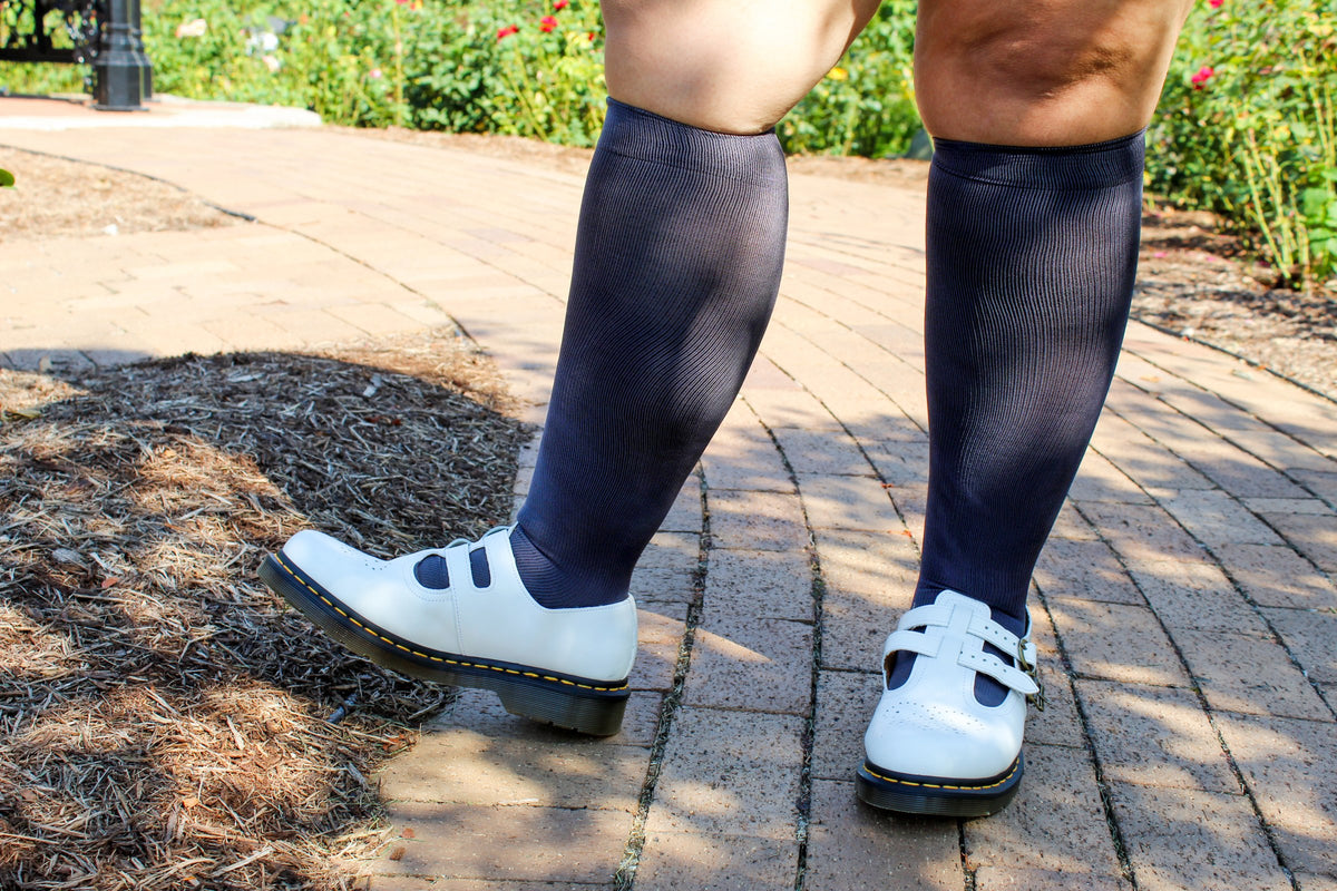 Woman wearing dark grey Dr. Motion wide calf knee-high compression socks with white shoes on a garden path