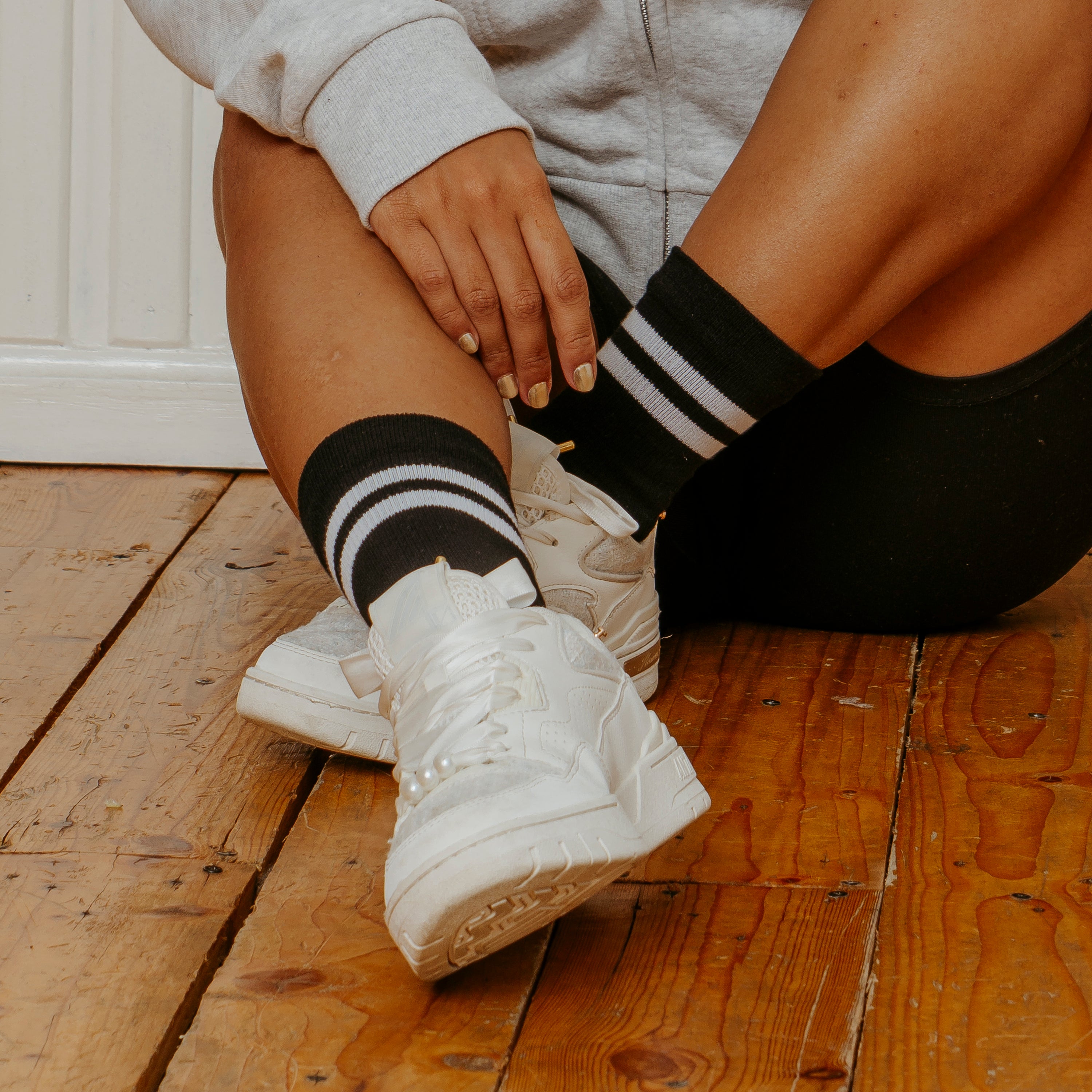 Mid-crew compression socks with double black and white stripes, worn with white sneakers on a wooden floor.