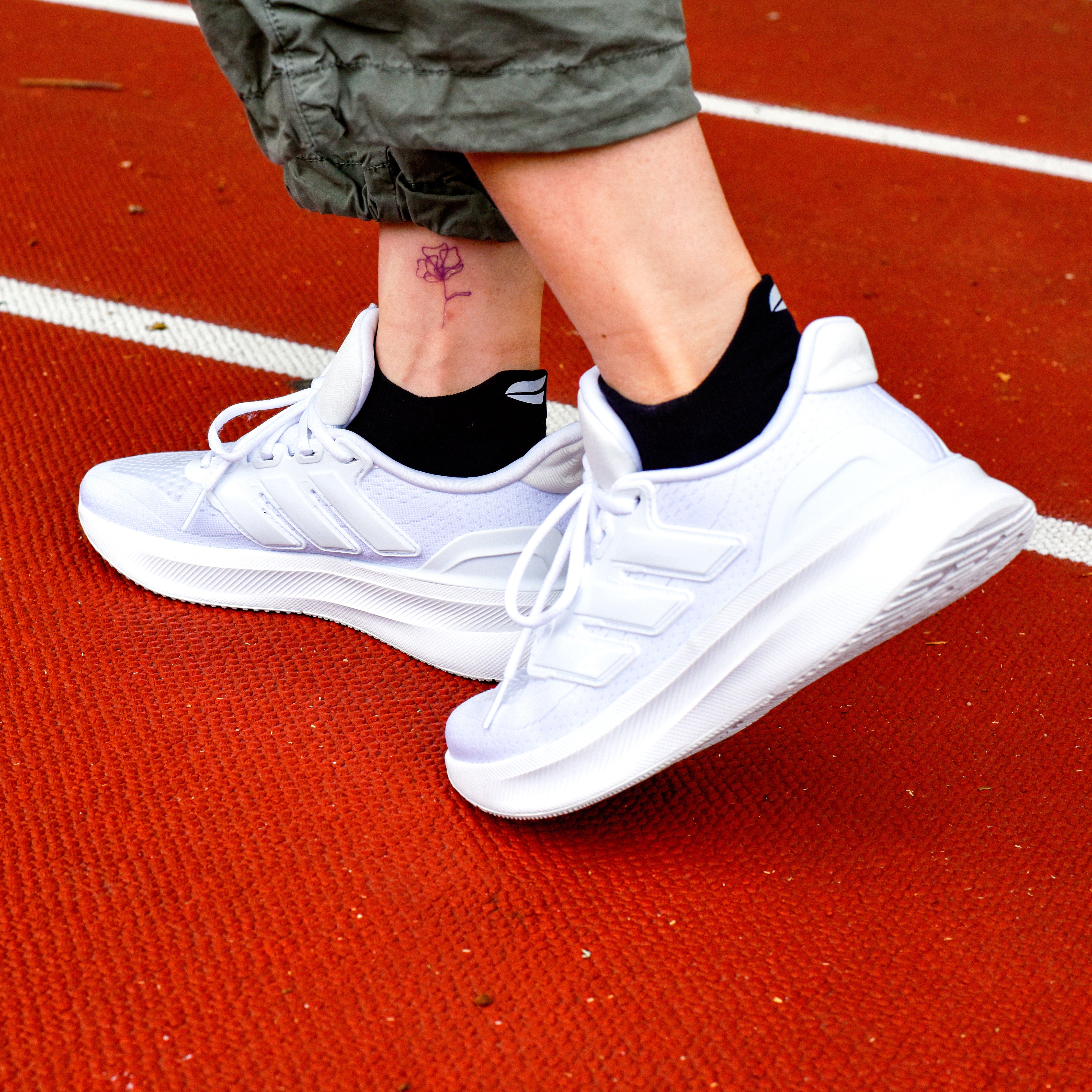Ankle compression socks in black worn with white athletic shoes on a red track surface.