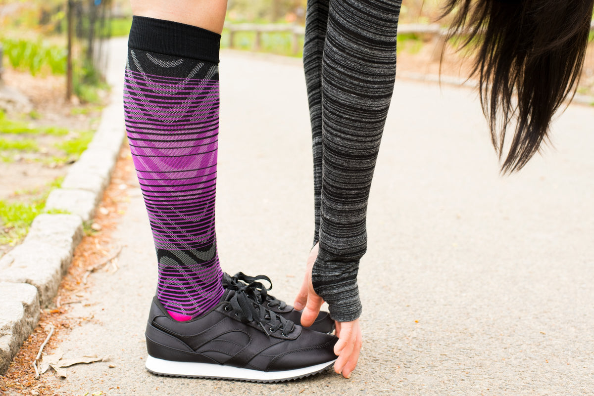 Woman stretching on a park path in purple Ombre Waves Dr. Motion sports compression socks