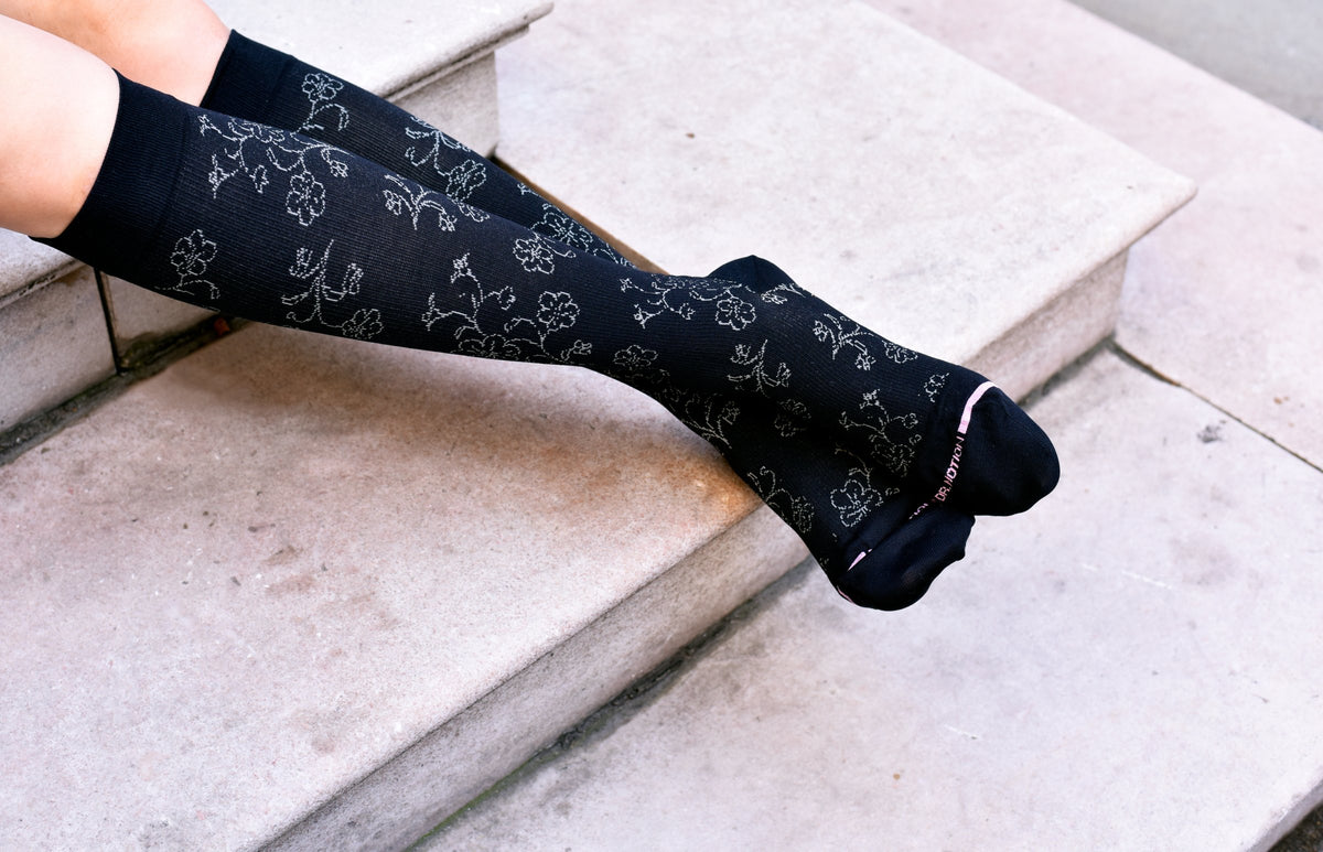 Woman resting her legs on stone steps in black floral Dr. Motion knee-high compression socks