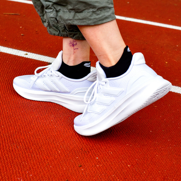 Ankle compression socks in black worn with white athletic shoes on a red track surface.