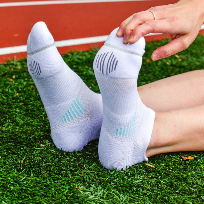 White ankle compression socks with textured patterns, worn on feet resting on green turf.