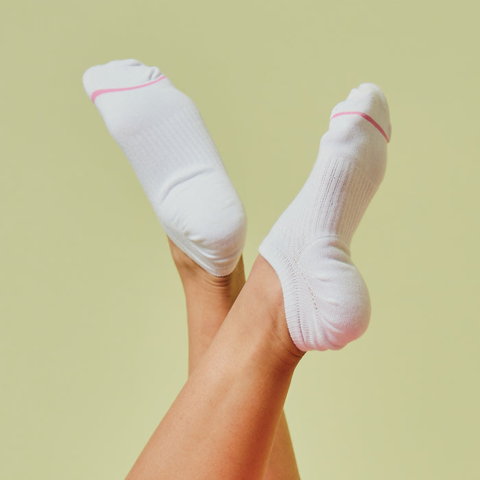 White liner compression socks with pink accents, displayed on raised feet against a light green background.