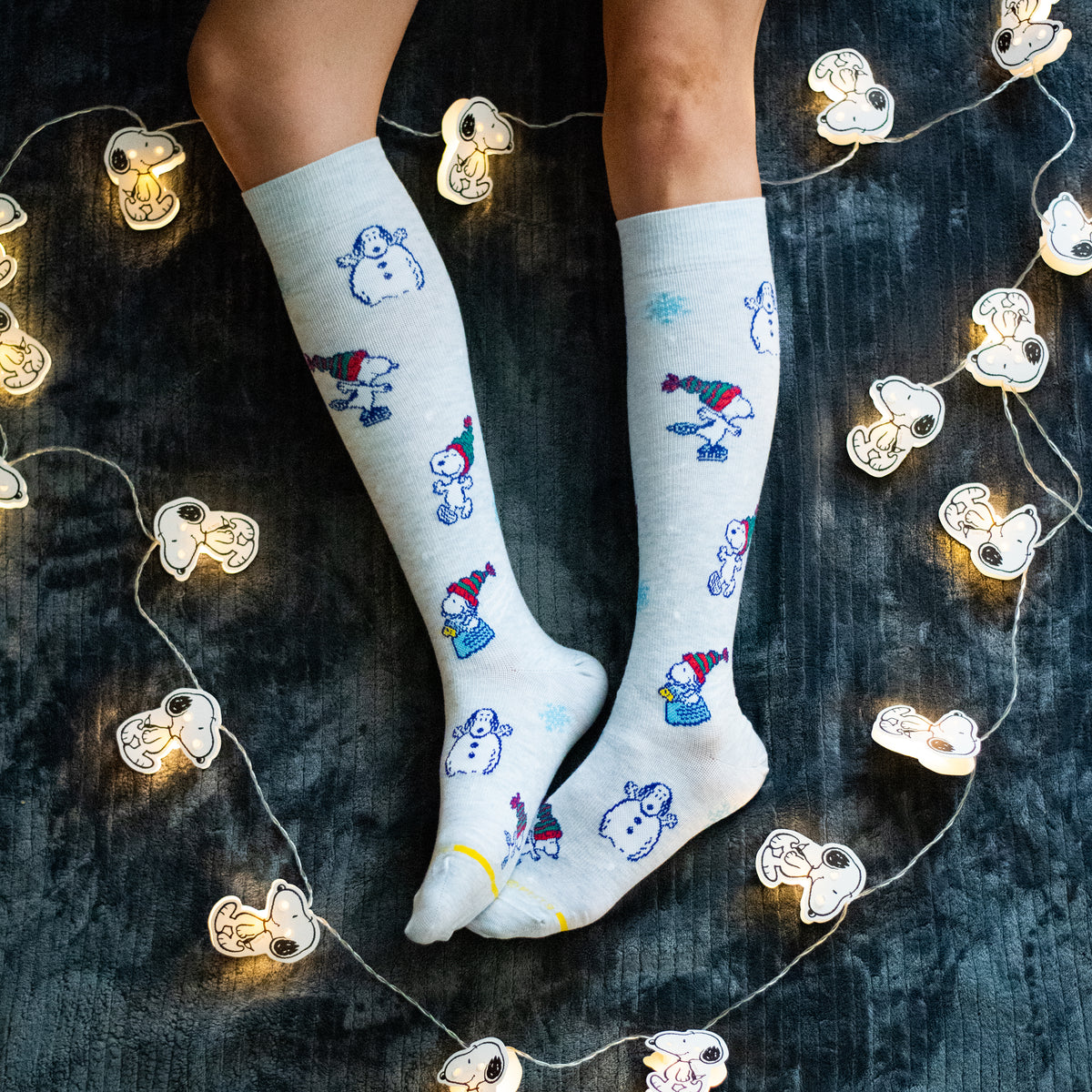 Pale blue heather knee-high compression socks with Snoopy winter designs, worn in a lifestyle setting.