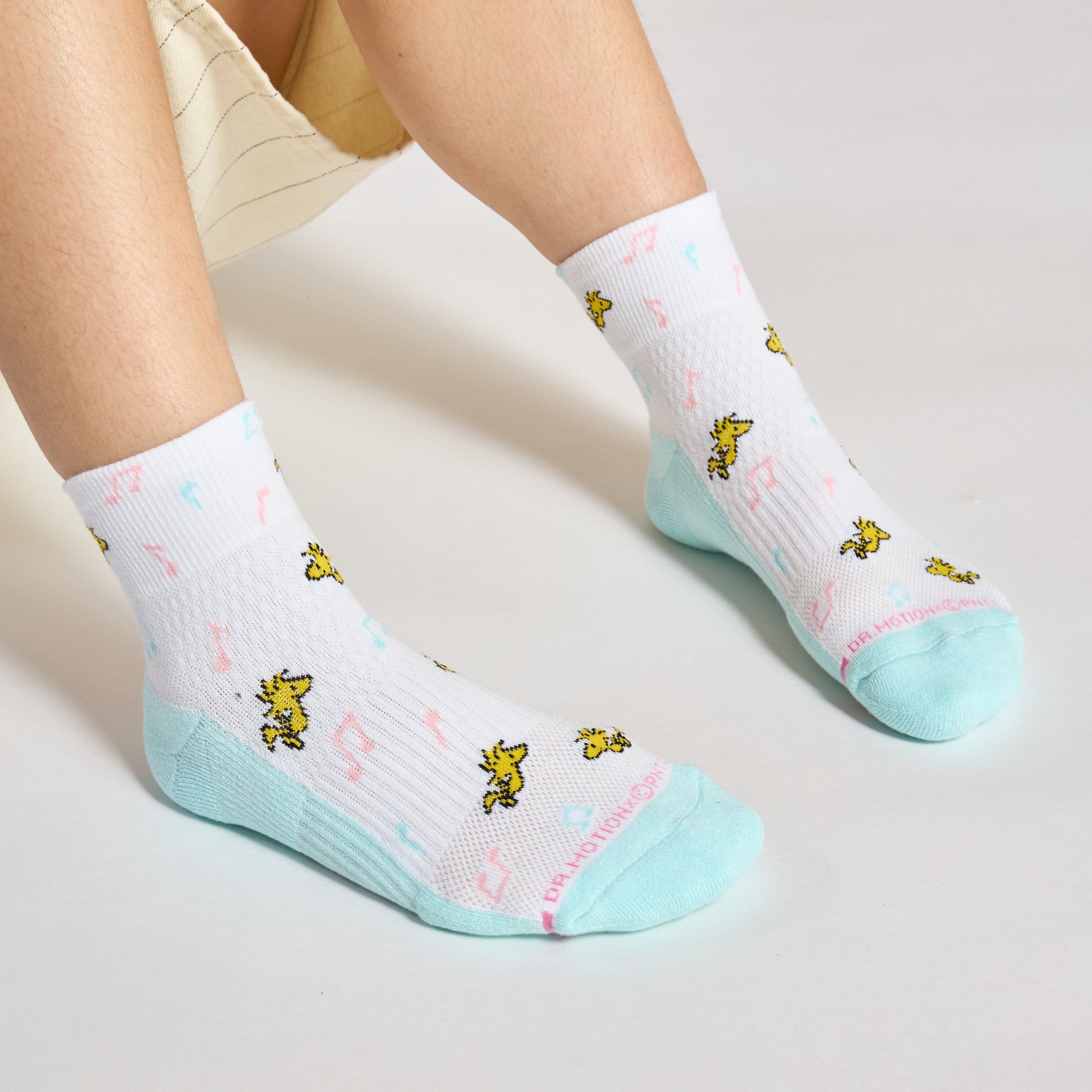 Quarter-length socks with a white base, featuring yellow characters and musical notes, with a mint green heel and toe.