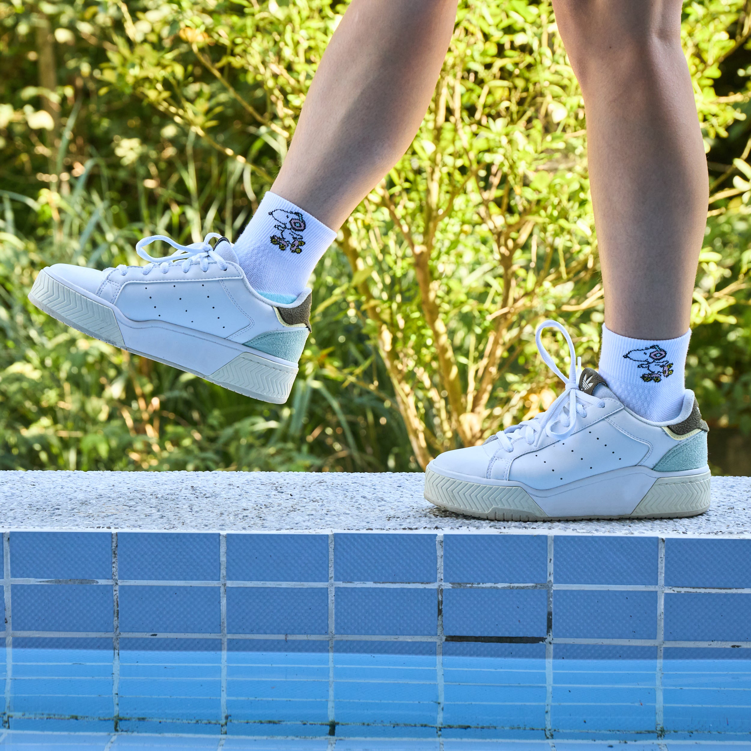 Quarter compression socks with Snoopy design worn with white sneakers, standing on a ledge by a pool.